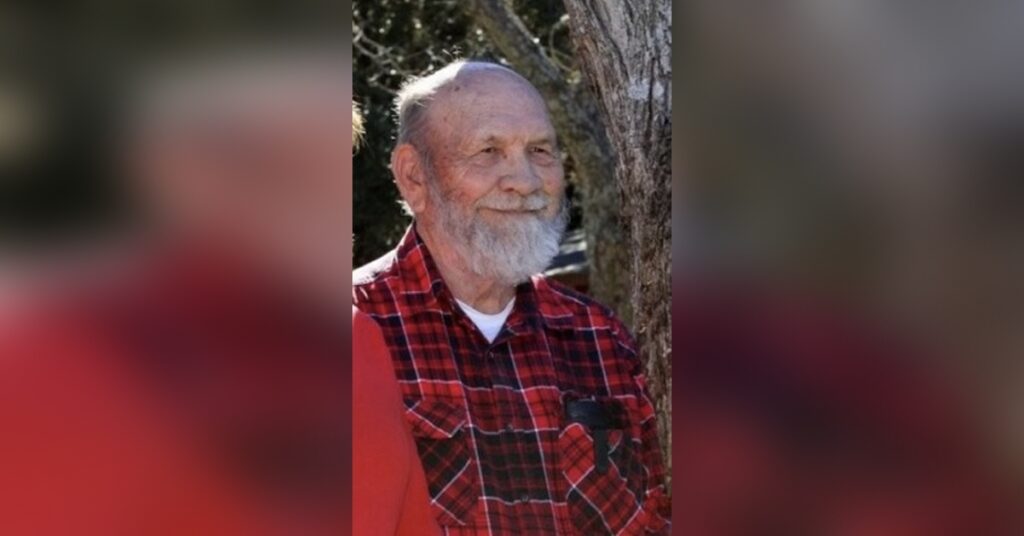 an Elderly John Eddie Vogt in a Red Plaid Shirt Standing Outdoors with a Gentle Smile, Embodying Wisdom and Nostalgia.