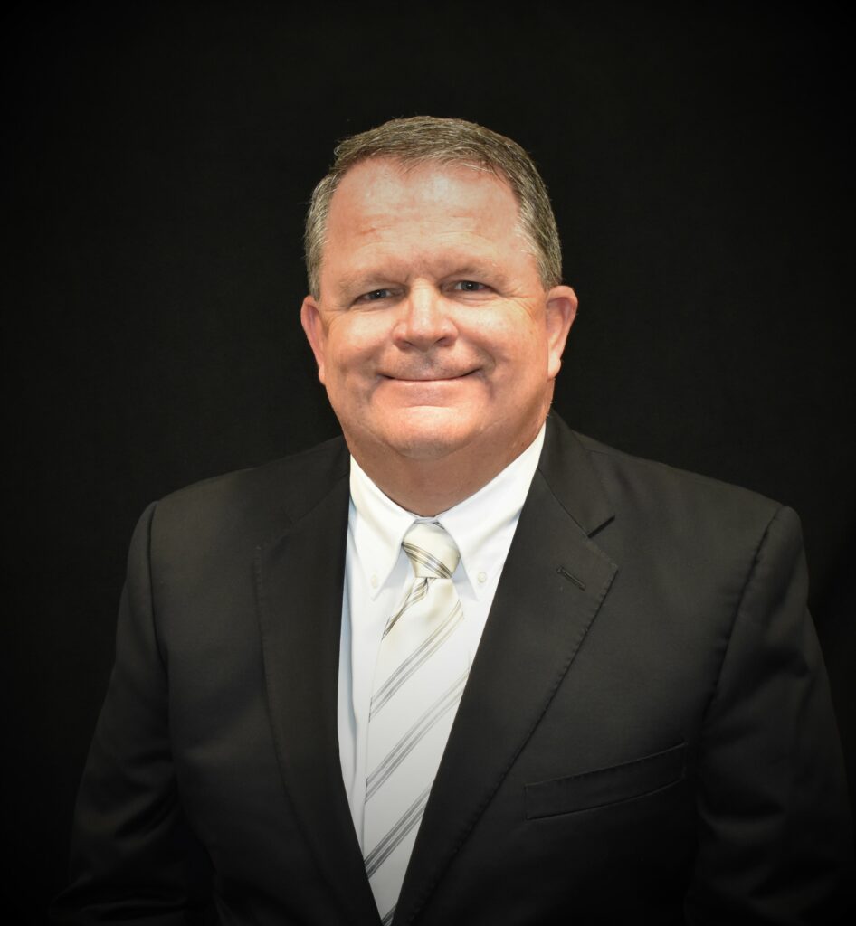 Coach Stan Leech – Leadership, Faith, and Basketball - the Kendall Gentleman Portrait of Coach Stan Leech in a Black Suit and Striped Tie, Smiling Confidently Against a Black Backdrop.