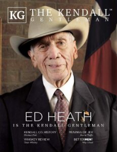 A portrait of Ed Heath, a distinguished older gentleman in a cowboy hat and suit, featured on the cover of The Kendall Gentleman magazine's March 2025 issue. The Texas flag and a framed Masonic certificate are in the background.