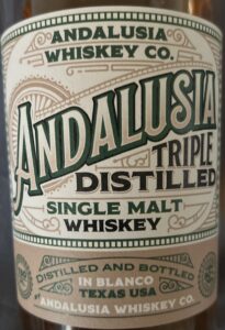 Close-up of an Andalusia Triple Distilled Single Malt Whiskey bottle label, highlighting its Texas origin and crafted quality.