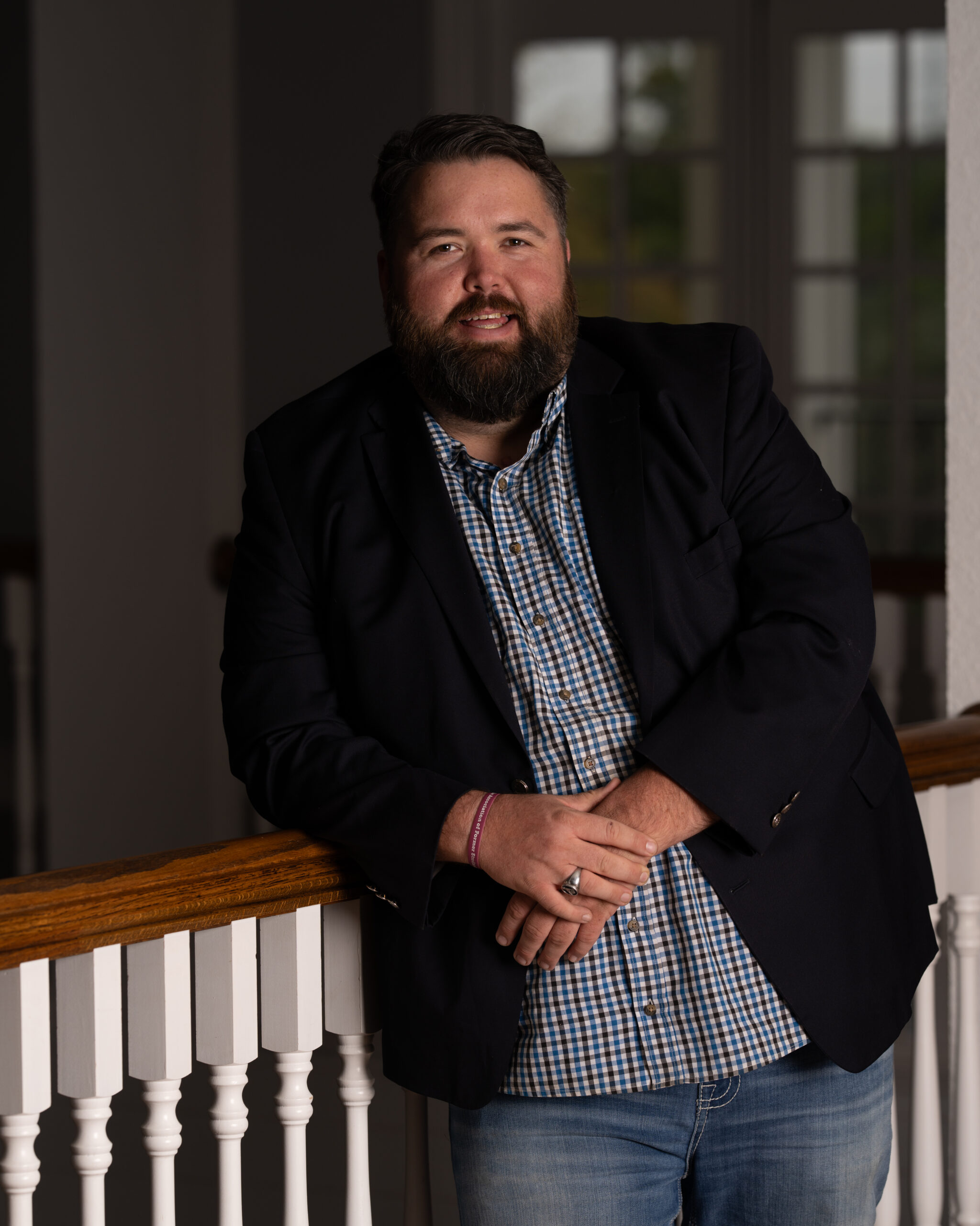 Michael Ethridge, Publisher of the Kendall Gentleman, Leaning on a Wooden Railing in a Blue Blazer and Checkered Shirt, Representing Modern Masculinity, Tradition, and Craftsmanship.