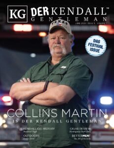 Collins Martin standing with arms crossed in front of firetruck lights, wearing a Texas cap on the June 2025 cover of The Kendall Gentleman magazine.