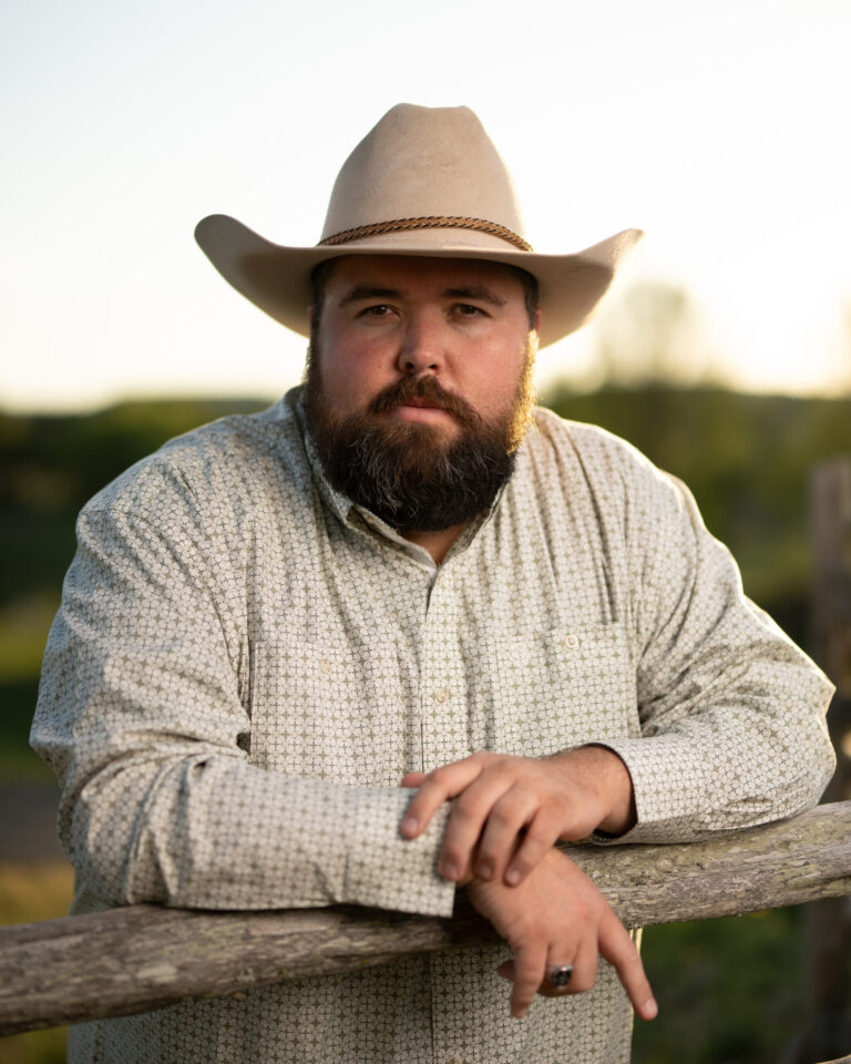 Michael G. Ethridge Stands at a Wooden Fence in the Texas Hill Country, Wearing a Cowboy Hat and a Thoughtful Expression.