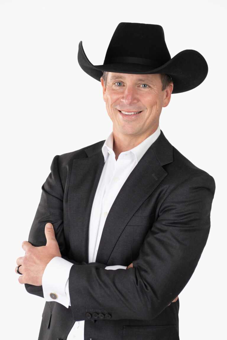 Sam Mcgee in a Dark Suit and Cowboy Hat, Smiling Confidently in a Professional Studio Portrait.