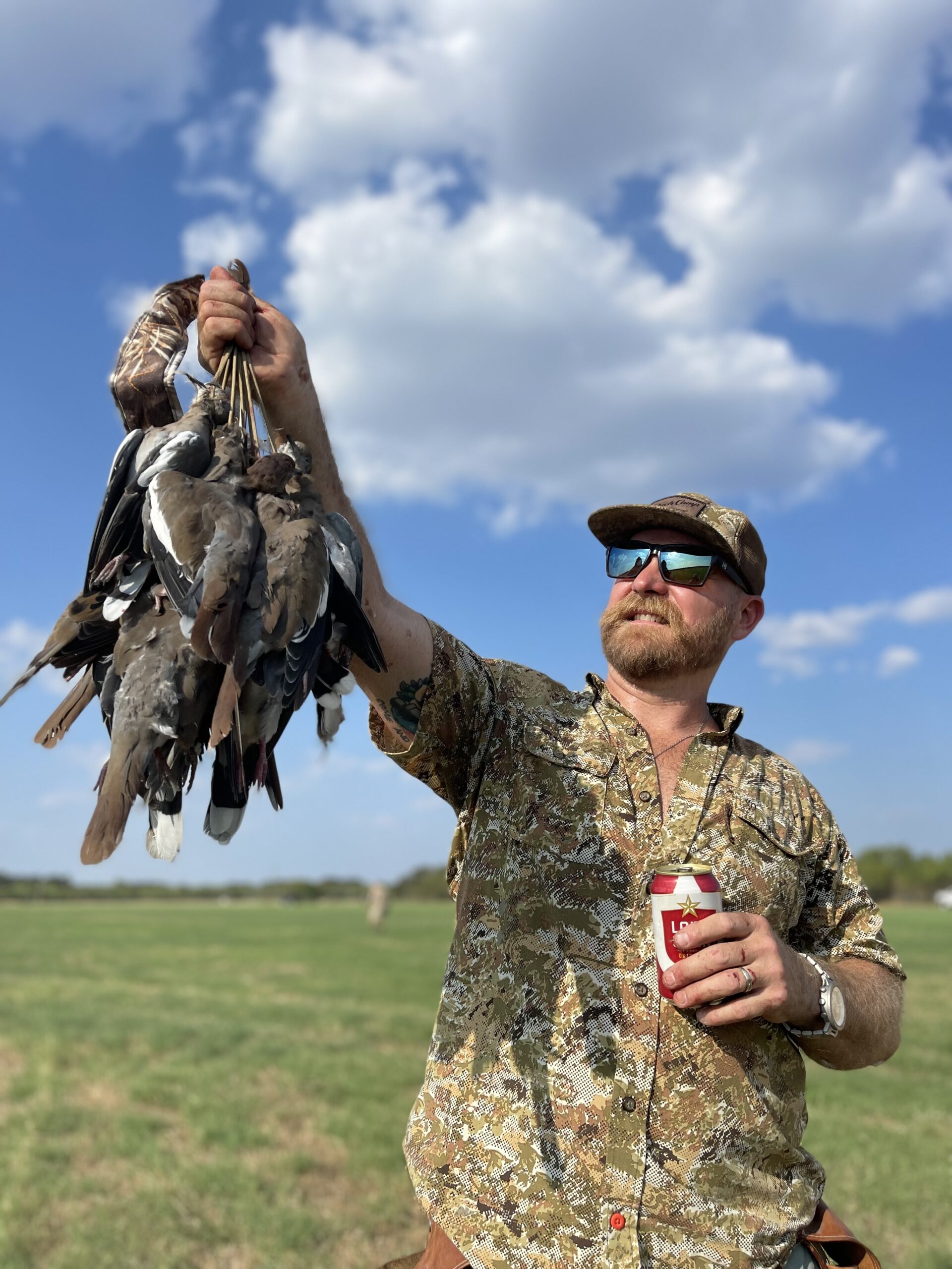 Jed Mazour Holds Up a String of Doves in a Texas Field During Dove Season, Enjoying a Lone Star Beer Under a Bright Hill Country Sky.