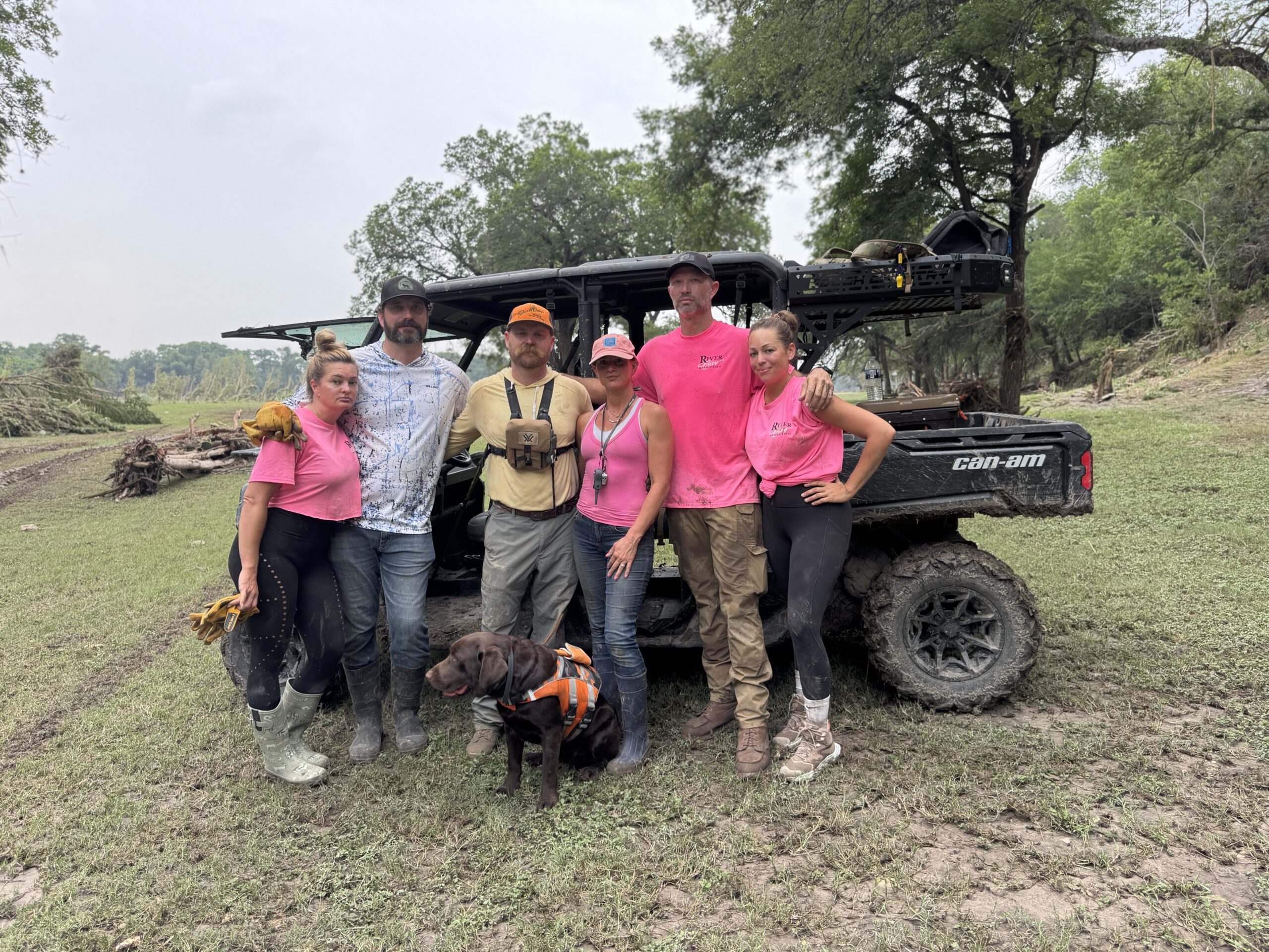 Volunteers from River Rev Stand Together After a Flood Cleanup Mission Near the Guadalupe River, Wearing Work Clothes and Muddy Boots Beside a Can-am Vehicle.
