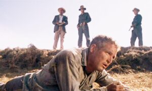 Paul Newman as Luke lies beaten but unbroken in the dirt, with prison guards watching from above in a scene from Cool Hand Luke.