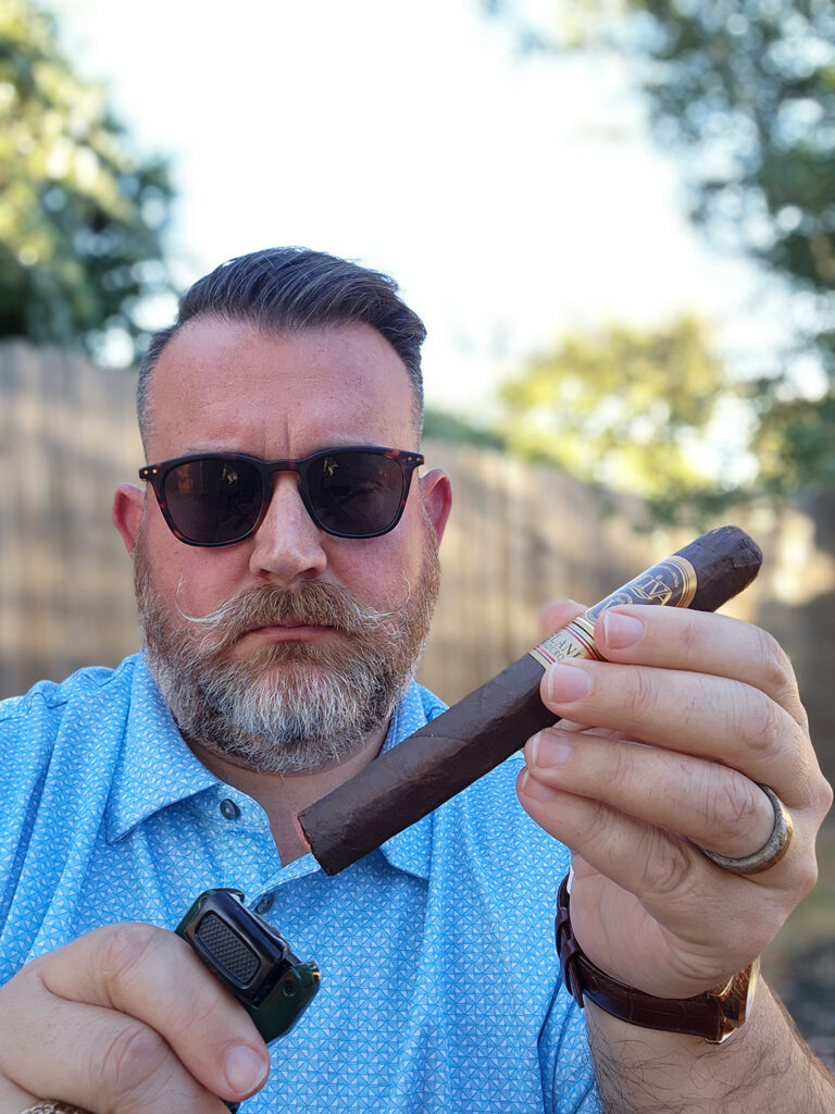 Clay Smoot Holds an Oliva Serie V Melanio Maduro Cigar and Lighter, Ready to Enjoy His Featured December Cigar Review.