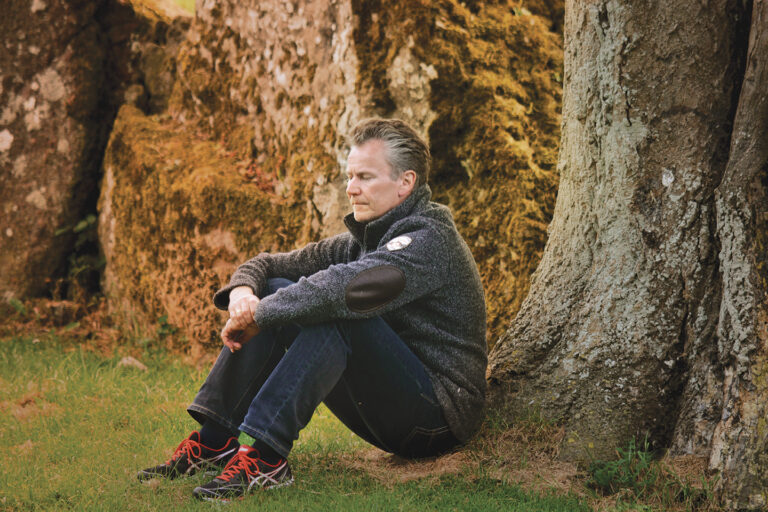 Man Sitting Thoughtfully Against a Tree in a Natural Outdoor Setting with Rock Formations in the Background.