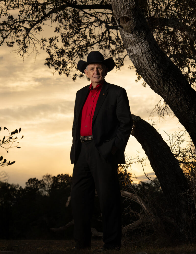 General Leroy Sisco standing outdoors at sunset wearing a black cowboy hat and red shirt, representing a lifetime of military service and leadership.