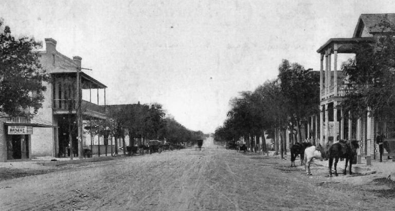 Historic photograph of early Boerne, Texas showing unpaved Main Street, storefronts, and horses in the late 19th century.