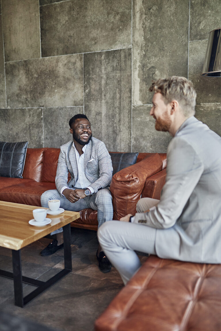 Two Well-dressed Men Seated in a Lounge Having a Thoughtful Conversation over Coffee, Representing Mentorship, Leadership, and Personal Growth
