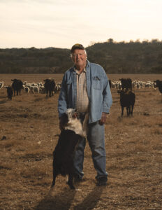 William “Bill” Whitworth standing on his Sisterdale ranch with cattle and sheep in Kendall County, Texas
