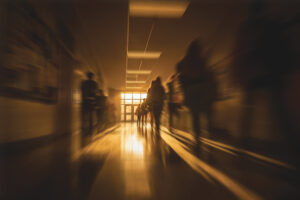 Blurred hallway scene with silhouetted figures walking through a school corridor at sunset, symbolizing uncertainty, growth, and the emotional challenges of young adulthood.