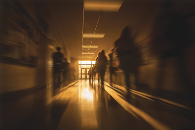 Blurred Hallway Scene with Silhouetted Figures Walking Through a School Corridor at Sunset, Symbolizing Uncertainty, Growth, and the Emotional Challenges of Young Adulthood.