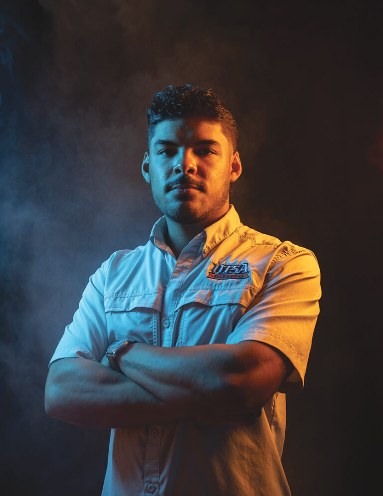 Portrait of Jordan Ballin Standing with Arms Crossed Under Dramatic Blue and Amber Lighting, Featured As the Cover Story Subject for the Kendall Gentleman.
