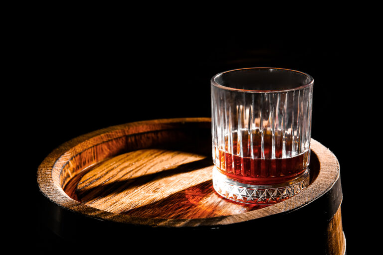 Glass of Aged Spirit Beside a Wooden Barrel, Representing Whiskey Education