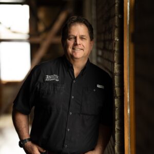 Tommy Mathews in a Black Work Shirt Inside a Brick Building