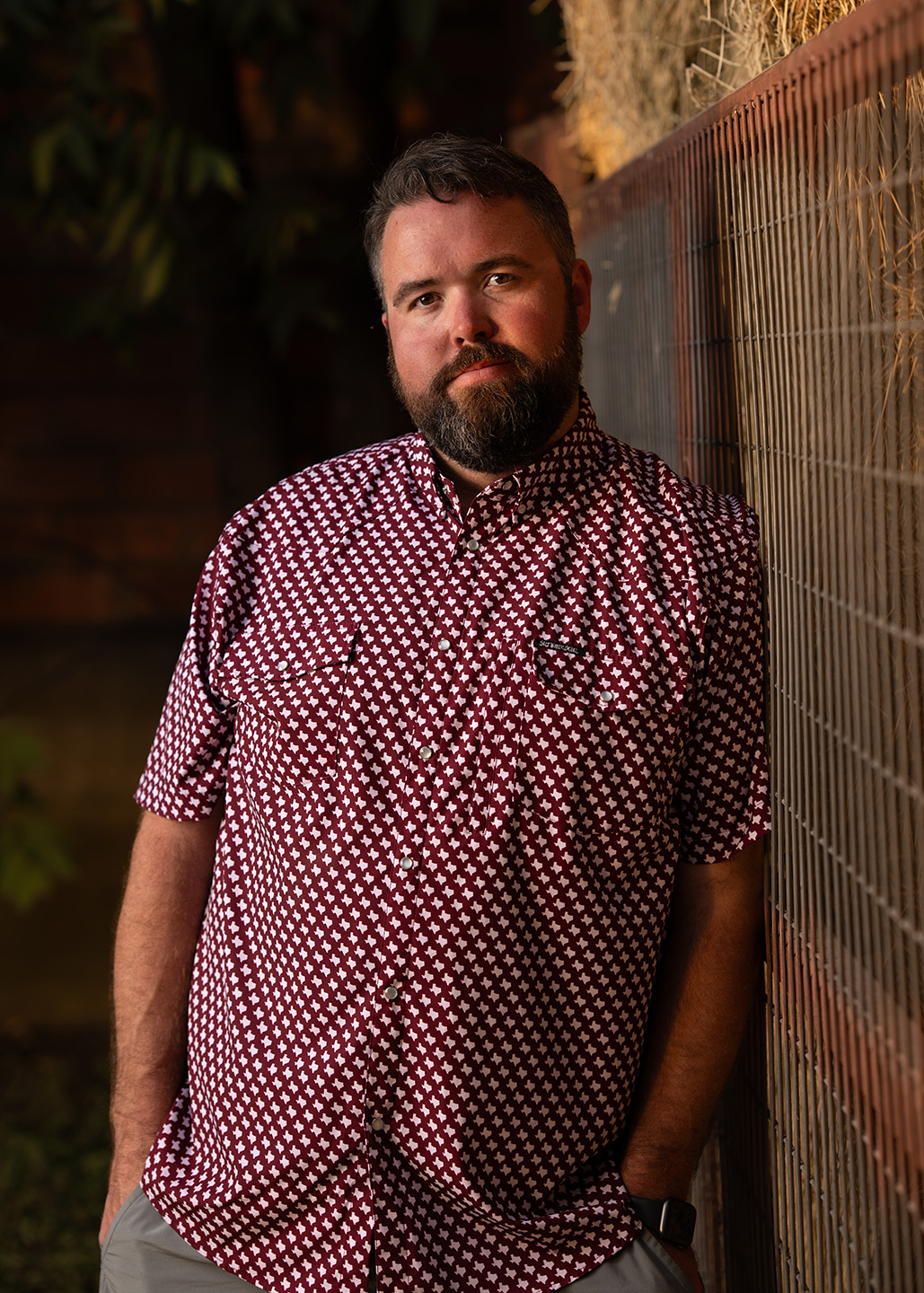 Michael G Ethridge, Publisher of the Kendall Gentleman, Leaning Against a Wire Fence in a Maroon Patterned Shirt